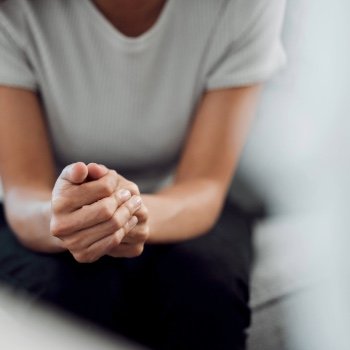 A female sitting on a couch across from her therapist leaning in with her one hand in the other.